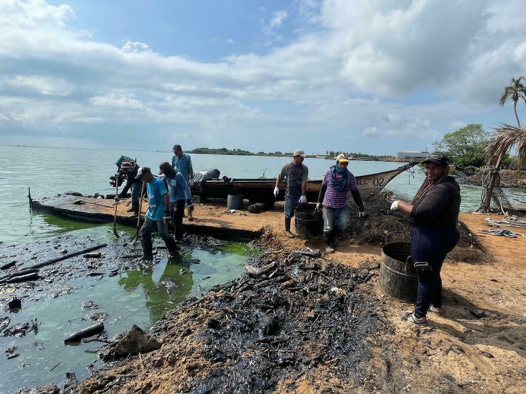 caption: A work brigade sponsored by Venezuelan state-run oil company PDVSA, which critics blame for the oil spills, use shovels and rakes to remove congealed petroleum from a Lake Maracaibo beach.