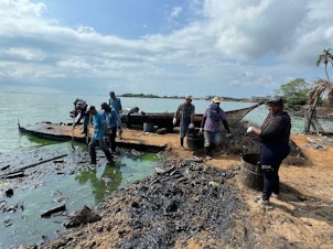 caption: A work brigade sponsored by Venezuelan state-run oil company PDVSA, which critics blame for the oil spills, use shovels and rakes to remove congealed petroleum from a Lake Maracaibo beach.