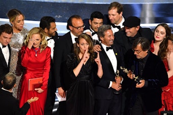 caption: The cast and crew of CODA accept their award onstage.