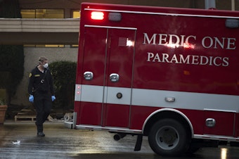 caption: Kirkland Fire Captain Seth Buchanan walks toward an ambulance before a patient from the Life Care Center of Kirkland was transported to Evergreen Health Medical Center on Monday, March 2, 2020, in Kirkland.