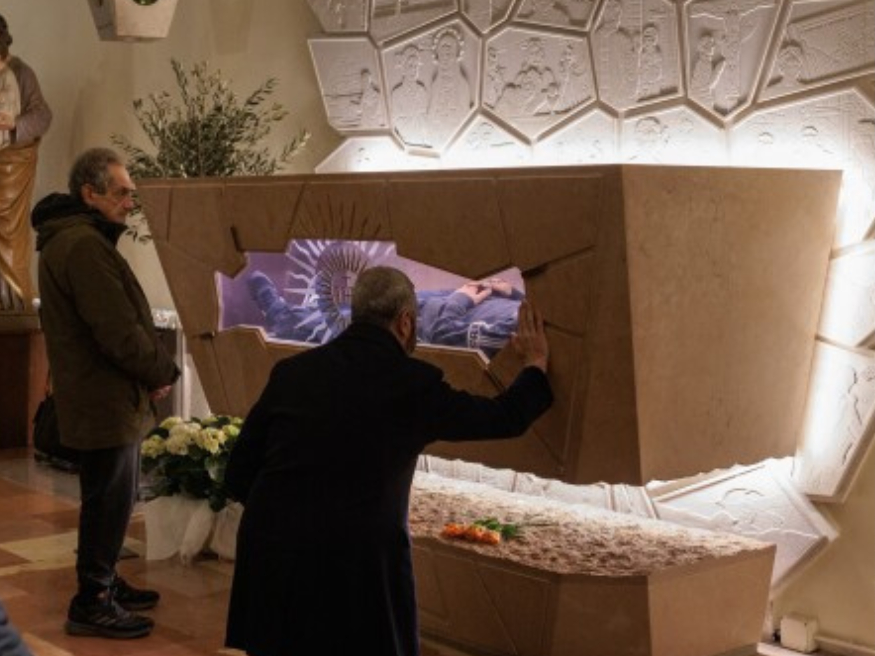 caption: The remains of Carlo Acutis have rested since April 6, 2019, in the Sanctuary of the Spoliation in St. Mary Major Church in Assisi, inside a sepulchral monument in the right nave. The body, after being transferred from its previous burial in a cemetery, was prepared through preservation techniques to be displayed to the faithful, who come to venerate him in this important place of worship.
