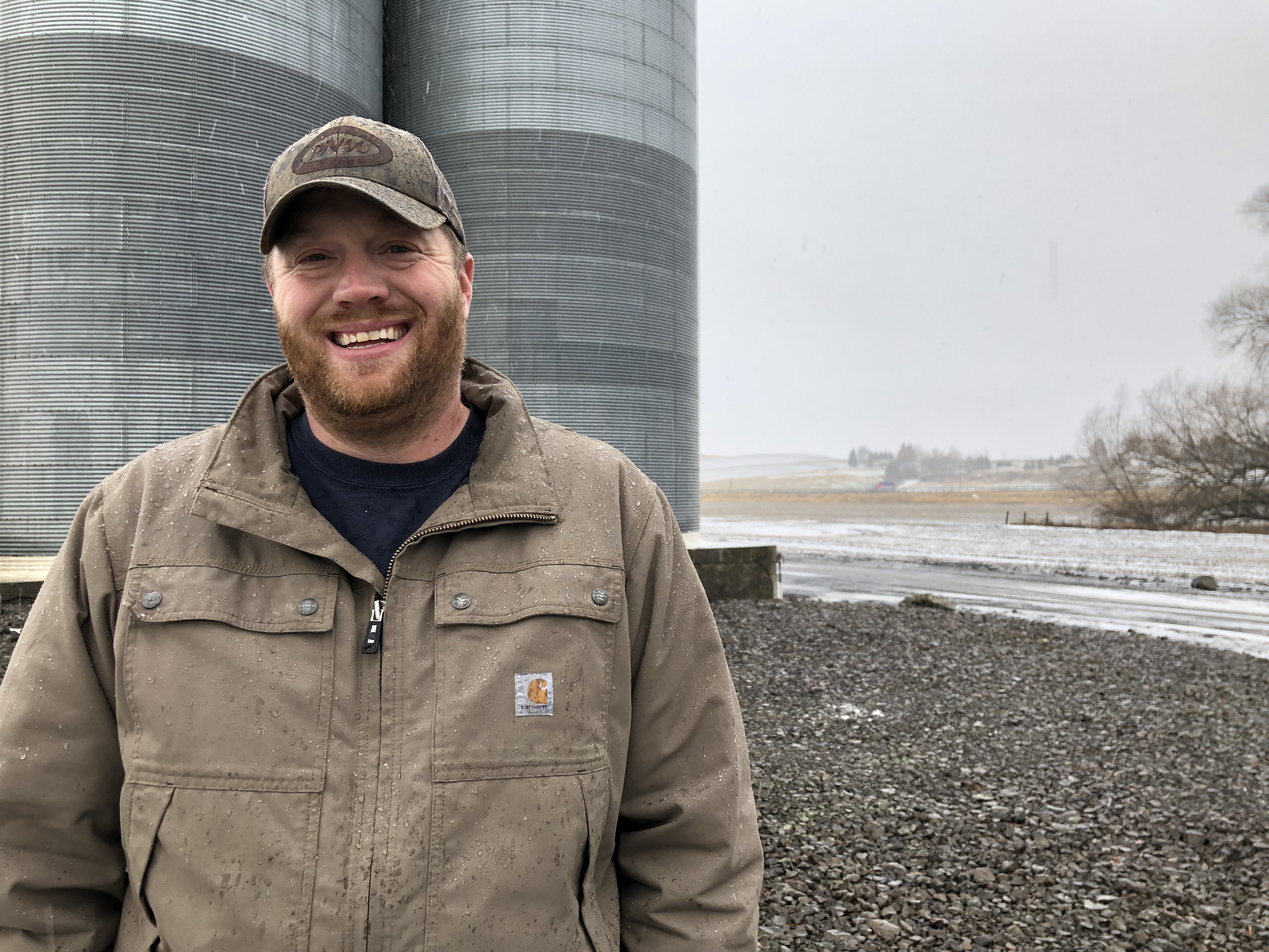 caption: Allen Druffel, 34, of Colton, Wash., stands in front of the co-op silos that hold his unsold chickpeas. Last year he was getting 50 cents a pound for his pulse crop. Now, the going price is 18 cents a pound — well below his cost of production.