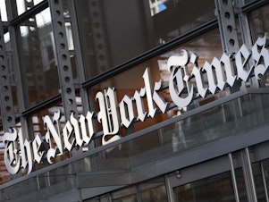 caption: A sign for The New York Times hangs above the entrance to its building on May 6, 2021 in New York.