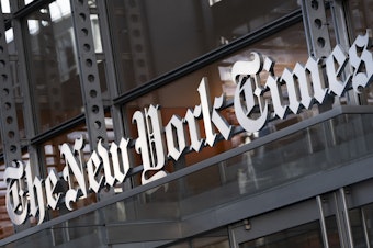 caption: A sign for The New York Times hangs above the entrance to its building on May 6, 2021 in New York.
