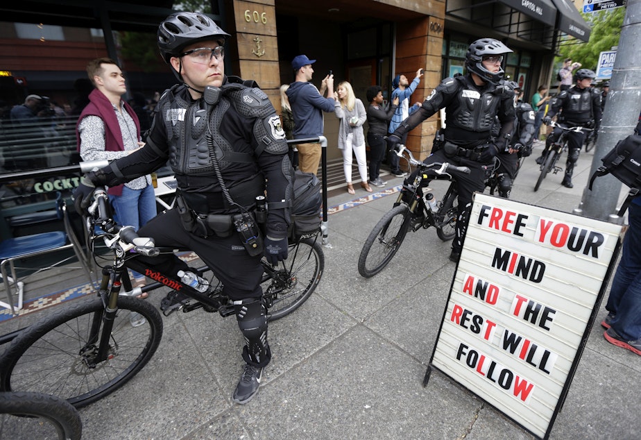 caption: Police officers pause next to a sign outside a restaurant as they observe a May Day anti-capitalism march, Friday, May 1, 2015 in Seattle.