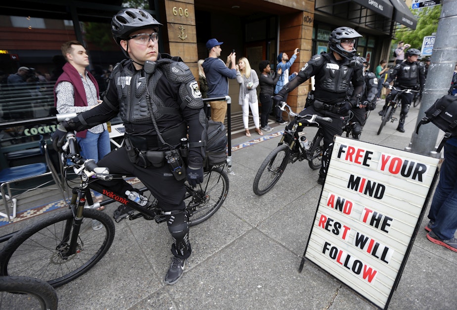 caption: Police officers pause next to a sign outside a restaurant as they observe a May Day anti-capitalism march, Friday, May 1, 2015 in Seattle.