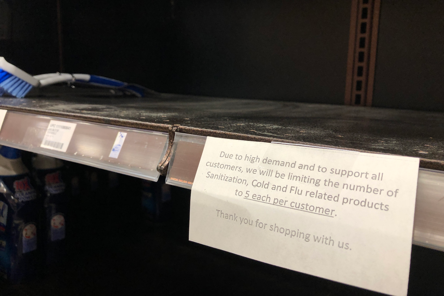 caption: Shelves at a Seattle grocery store are mostly empty of cleaning supplies. A sign states that customers are limited to five items. 