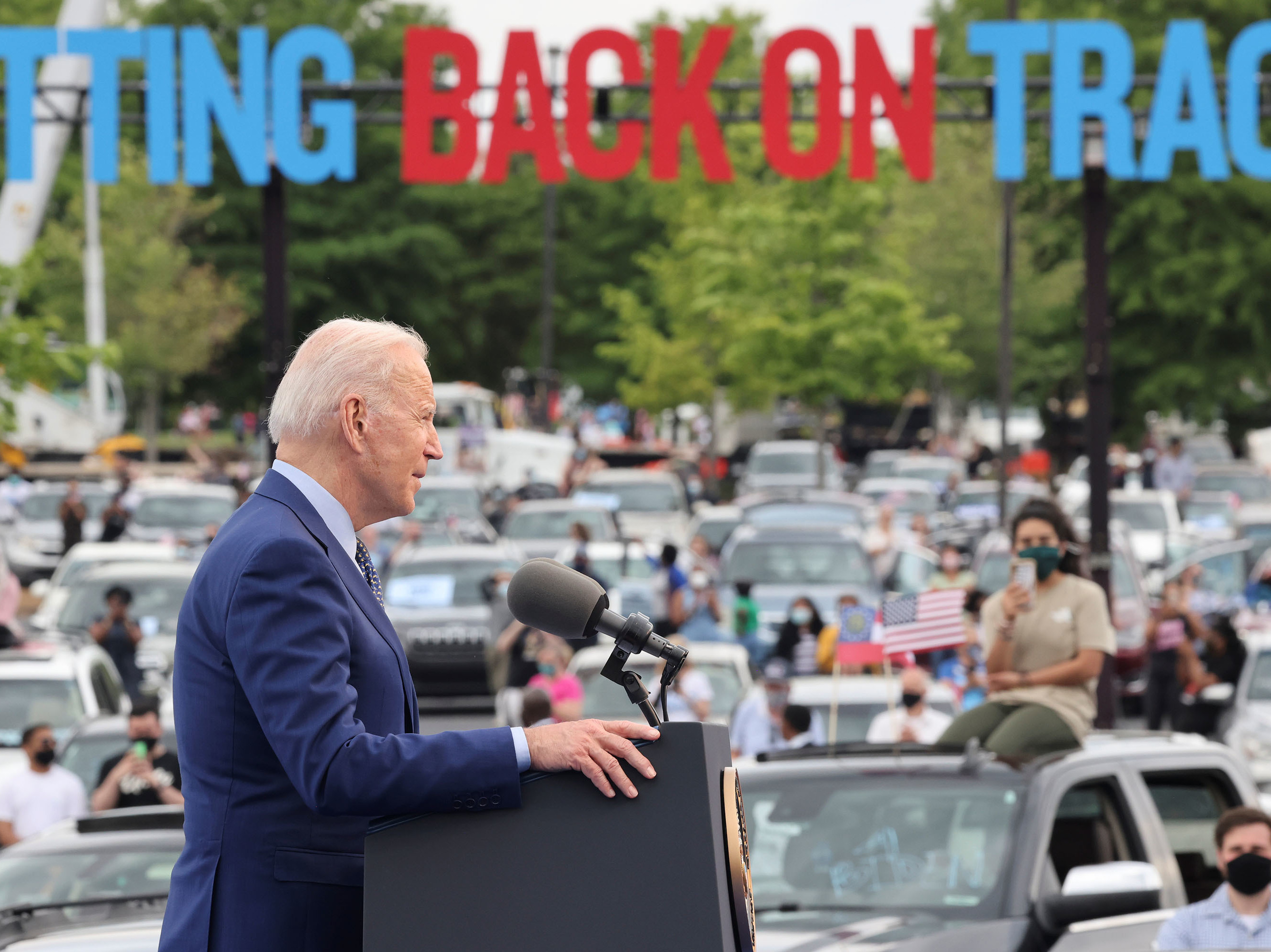caption: President Joe Biden speaks during the Democratic National Committee's "Back on Track" drive-in car rally in Duluth, Georgia, to celebrate his 100th day in office. Immigrant advocates were there to protest.