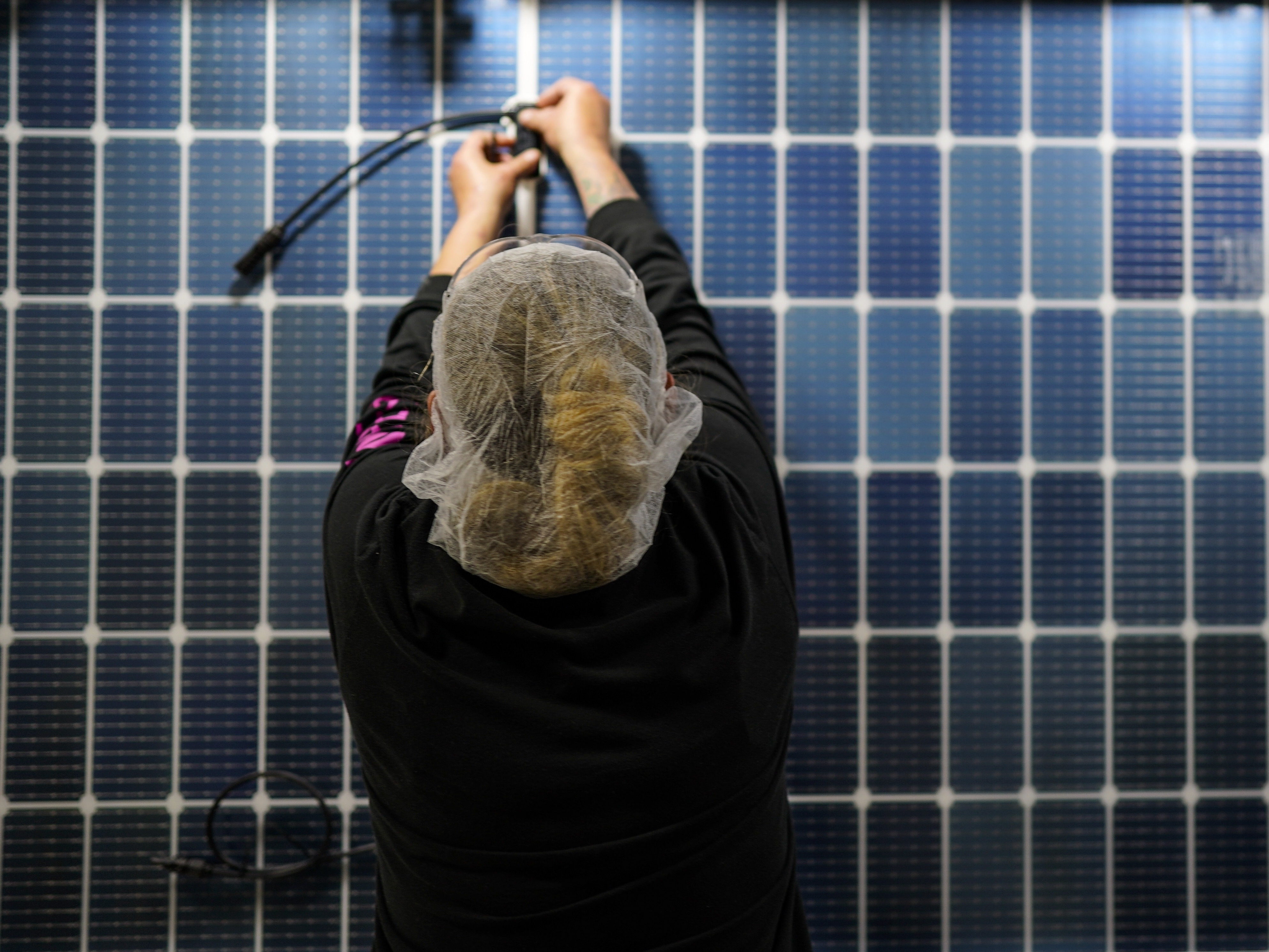 caption: An employee works on a solar panel inside a Qcells factory in Dalton, Ga.