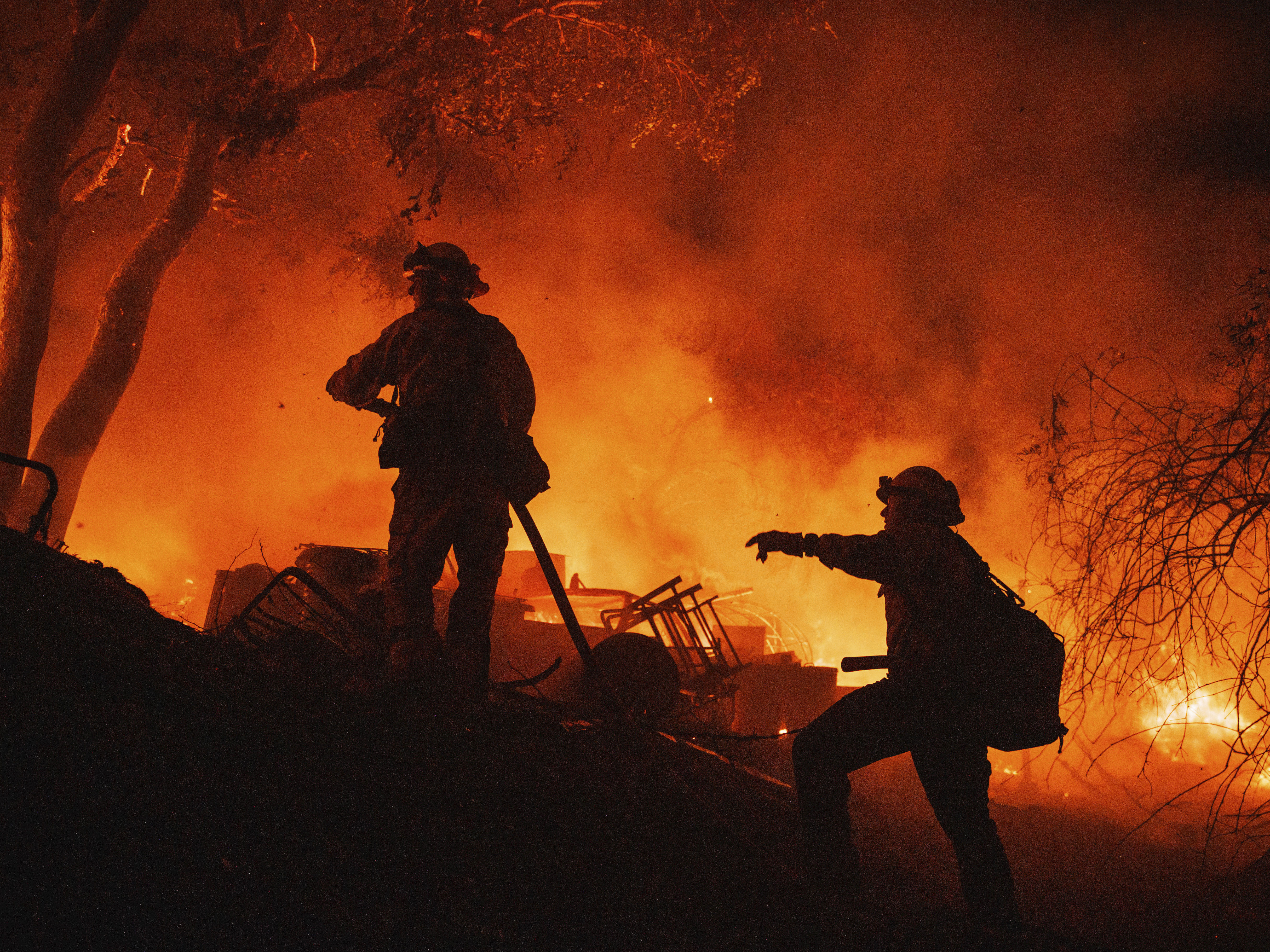 caption: Firefighters coordinate efforts at a burning property while battling the Fairview Fire on Monday, near Hemet, Calif.