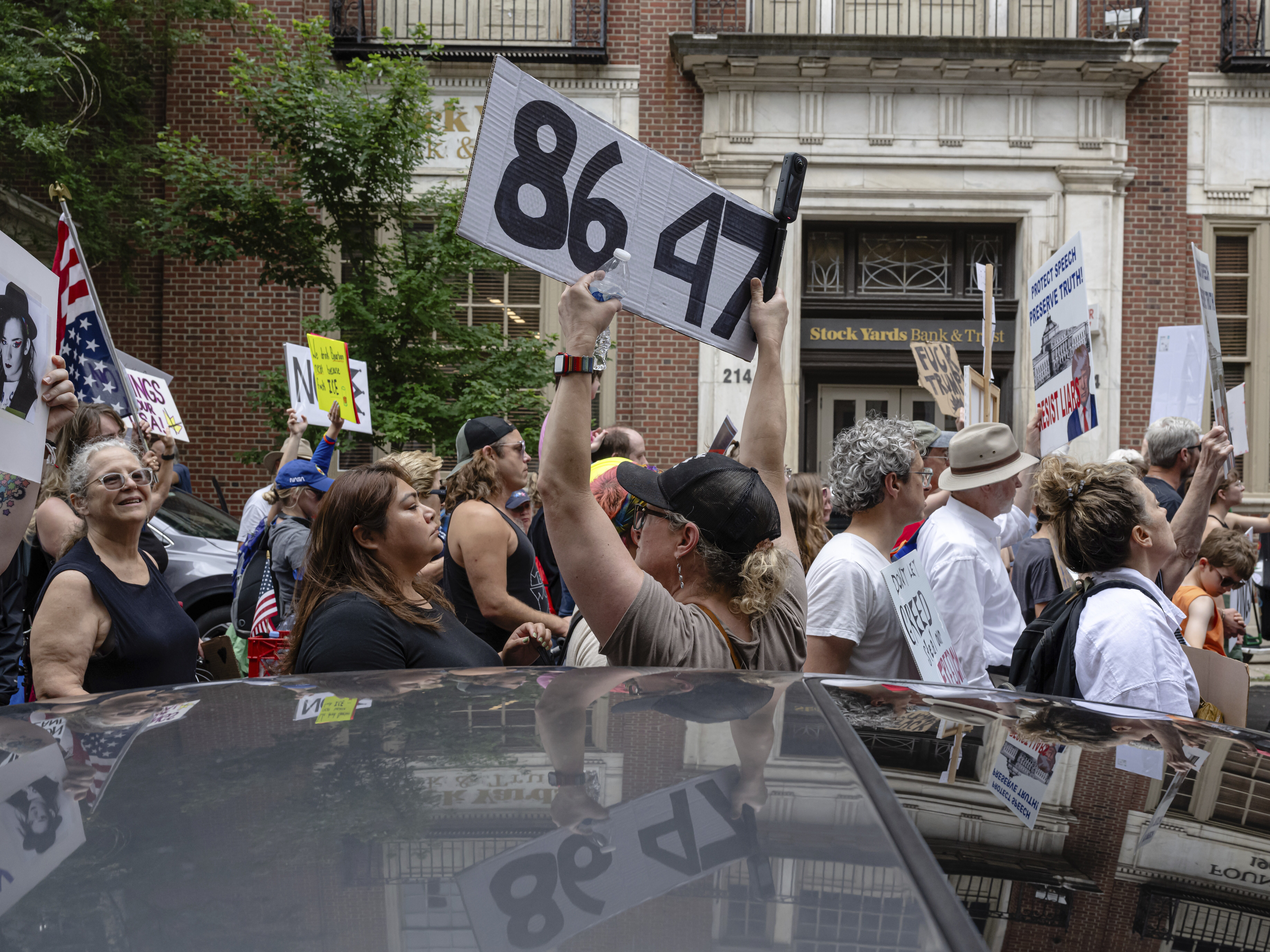 caption: A demonstrator holds up an "8647" sign at a "No Kings" protest in Louisville, Ky., in June 2025. It's an anti-Trump slogan, with multiple interpretations.