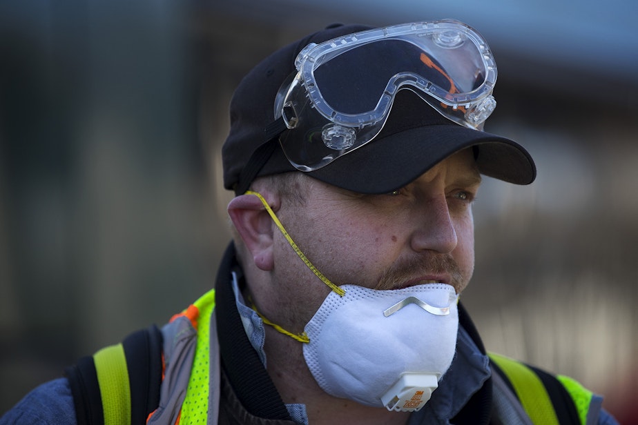 caption: Larry Bowles, an equipment service worker with King County Metro, wears a mask and goggles ahead of spraying a Virex II cleaning solution on the interior of a King County metro bus on Wednesday, March 4, 2020, at the Atlantic Base on 6th Avenue South in Seattle. 