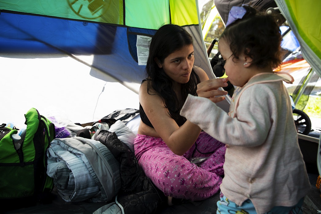 caption: Brithany, of Venezuela, feeds her 1.5-year-old daughter inside their tent on Wednesday, May 1, 2024, at Powell Barnett Park in Seattle. Brithany says their family is in desperate need of clothing. 