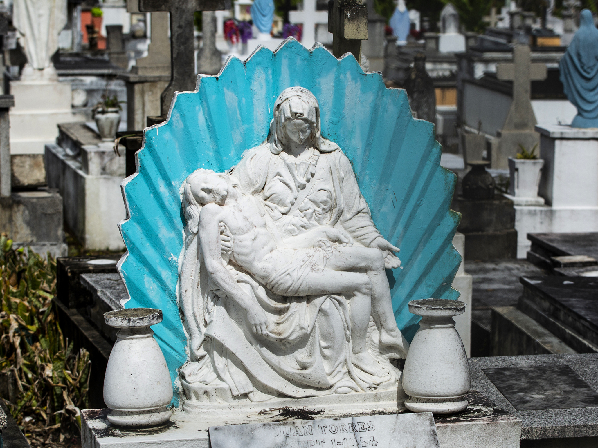 caption: Virgin Mary statue at the Lares Municipal Cemetery. The landslide caused by Hurricane Maria damaged nearly 1,800 tombs, uprooting caskets from their graves and sending some of them tumbling down a hillside.