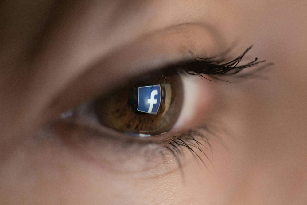 caption: An illustration picture taken on March 22, 2018 in Paris shows a close-up of the Facebook logo in the eye of an AFP staff member posing while she looks at a flipped logo of Facebook. (CHRISTOPHE SIMON/AFP via Getty Images)
