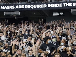 caption: Raiders fans do the wave during last weekend's preseason game in Las Vegas as a stadium sign reminds them to wear face masks. The team now says spectators will have to show proof of vaccination — and that no masks will be required for those who have been vaccinated.