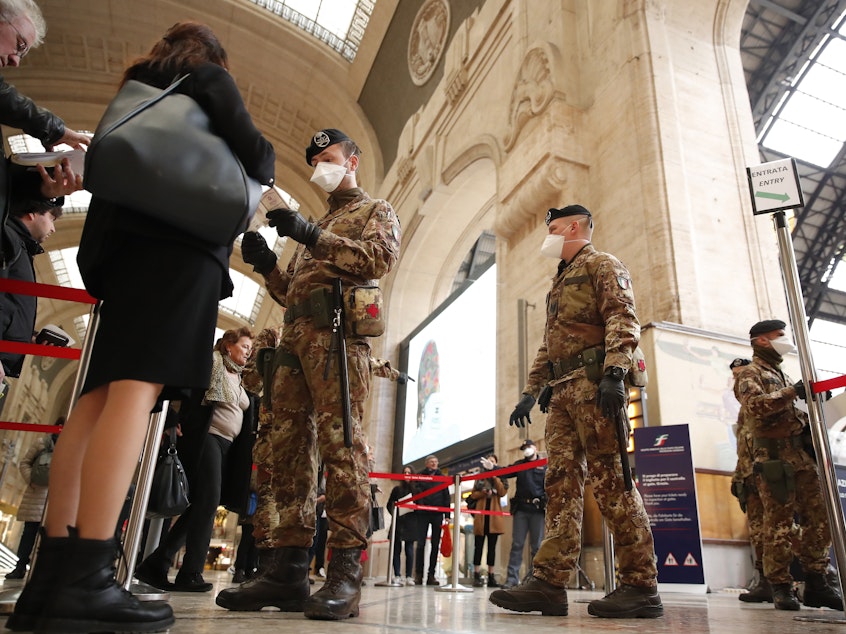 caption: Police officers and soldiers check passengers leaving from the main train station in Milan, Italy. The government declared on Monday that the whole country is a "red zone."