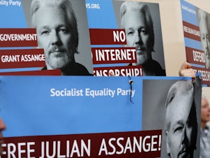 caption: Protesters carry posters depicting Julian Assange outside Westminster Magistrates Court in London on Thursday where the WikiLeaks founder appeared by video link from prison for an extradition hearing.