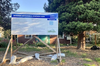 caption: A sign in front of the St Luke's Episcopal Church property in Ballard describes planned construction — an eight-story institution and apartment building.