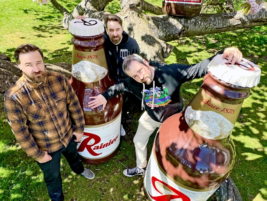 caption: "Rainier: A Beer Odyssey" makers (left to right) Justin Peterson, Rob Peterson and director Isaac Olsen pose with the iconic Beer with legs props from vintage Rainier ads. The trio of Tacomans digitized hundreds of reels of Rainier Beer advertising and behind the scenes footage in collaboration with the Washington State Historical Society. 