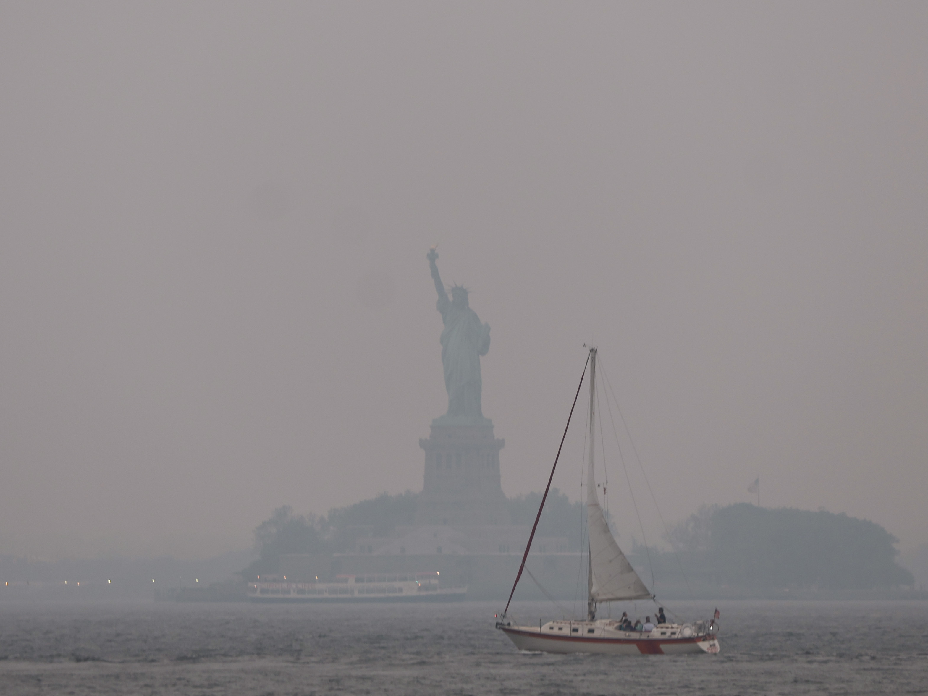 caption: The Statue of Liberty stands shrouded in a reddish haze as a result of Canadian wildfires on Tuesday.