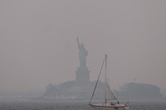 caption: The Statue of Liberty stands shrouded in a reddish haze as a result of Canadian wildfires on Tuesday.
