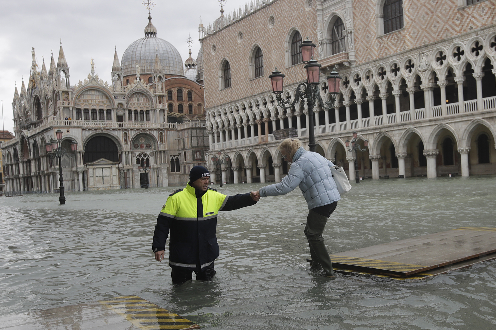 caption: A city worker helps a woman who decided to cross St. Mark square on a gangway, in spite of prohibition, in Venice, Italy, Sunday, Nov. 17, 2019. (Luca Bruno/AP)