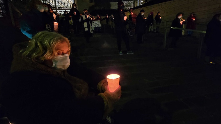 caption: Allene Steinberg holds a candle after calling on elected officials to provide more housing to homeless women. Tuesday, December 21, 2021.