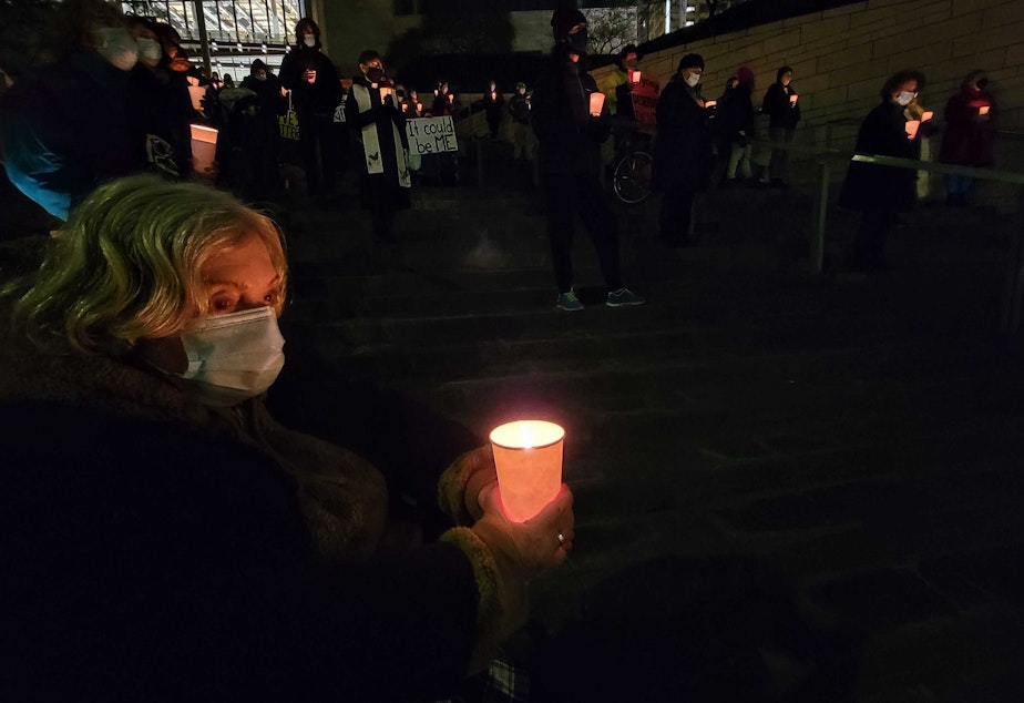 caption: Allene Steinberg holds a candle after calling on elected officials to provide more housing to homeless women. Tuesday, December 21, 2021.