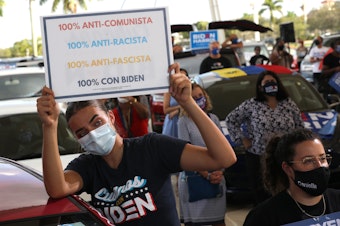caption: Wearing a face masks to reduce the risk posed by the coronavirus, Sophia Hildalgo (L) and Amore Rodriguez of Miami stay with their car decorated in Cubans for Biden paint as Democratic presidential nominee Joe Biden delivers remarks during a drive-in voter mobilization event at Miramar Regional Park October 13, 2020 in Miramar, Florida. (Chip Somodevilla/Getty Images)