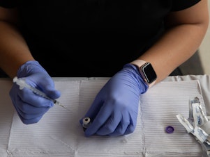 caption: A health care worker fills syringes with doses of the COVID-19 vaccine in August in Southfield, Mich.