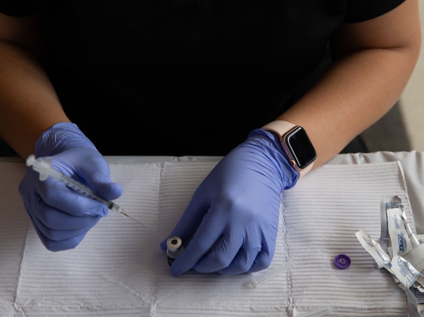 caption: A health care worker fills syringes with doses of the COVID-19 vaccine in August in Southfield, Mich.