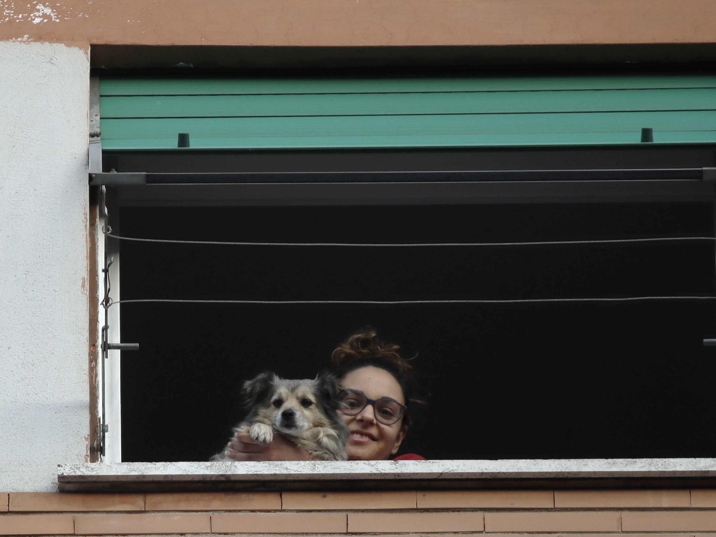 caption: A girl and her dog look out from a window during one of the many flash mobs taking place in Rome, on Sunday. The nationwide lockdown to slow coronavirus is still in its early days for much of Italy, but Italians are already showing signs of solidarity.
