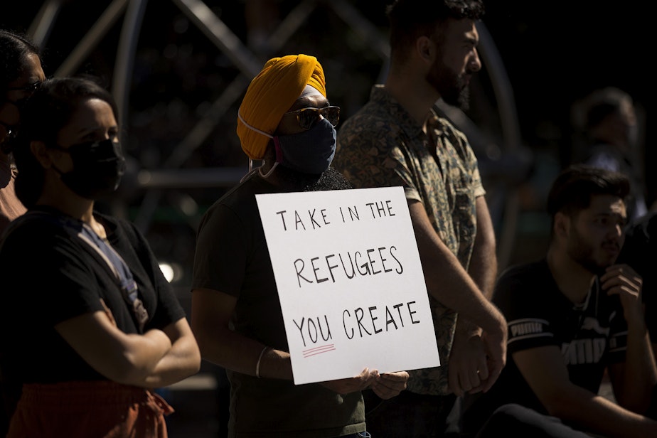 caption: Angad Singh holds a sign that reads, 'Take in the refugees you create,' while attending a rally and march in solidarity with Afghans on Saturday, August 28, 2021, at Westlake Park in Seattle. 