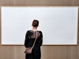 caption: A woman stands in front of an blank canvas hung up at the Kunsten Museum in Aalborg, Denmark, in 2021. Danish artist Jens Haaning sent the museum blank canvasses under the title <em>Take the Money and Run</em>.