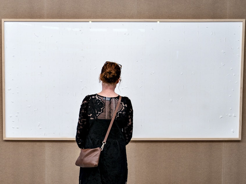 caption: A woman stands in front of an blank canvas hung up at the Kunsten Museum in Aalborg, Denmark, in 2021. Danish artist Jens Haaning sent the museum blank canvasses under the title <em>Take the Money and Run</em>.