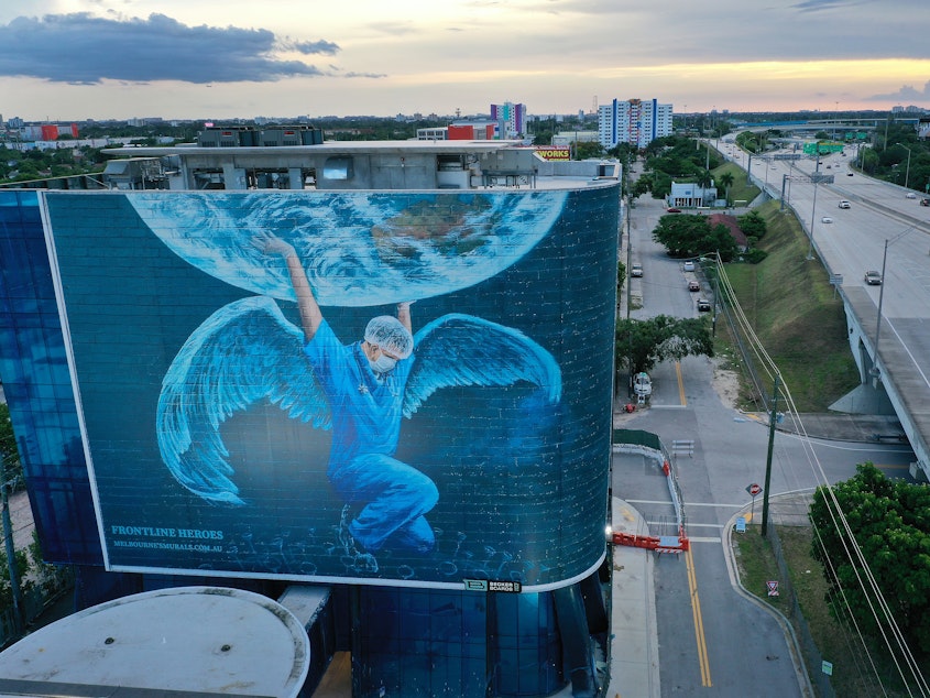 caption: A billboard in Miami — where coronavirus cases continue to surge — depicts a medical worker holding up the world. The number of coronavirus deaths worldwide has surpassed 600,000, with more than 140,000 of those in the U.S.