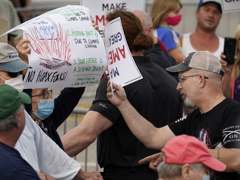 caption: At a Saco, Maine, campaign rally for President Trump in September, a protester holding a sign detailing the effects of climate change on the Gulf of Maine (left) came face to face with Trump supporters who had different views.
