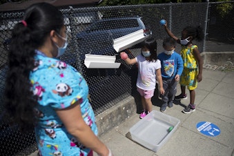caption: Students play a game with teacher Margarita Arias, left, on the playground after collecting flowers on a walk, on Thursday, July 16, 2020, at the Denise Louie Education Center along Beacon Avenue South in Seattle.