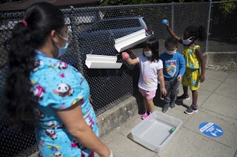 caption: Students play a game with teacher Margarita Arias, left, on the playground after collecting flowers on a walk, on Thursday, July 16, 2020, at the Denise Louie Education Center along Beacon Avenue South in Seattle.