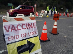 caption: Drivers with an appointment enter a COVID-19 vaccination site set up in the parking lot of Dodger Stadium in Los Angeles on Saturday. One of the largest vaccination sites in the country, it was temporarily shut down Saturday afternoon because of protesters, stalling hundreds of motorists who had been waiting in line for hours.