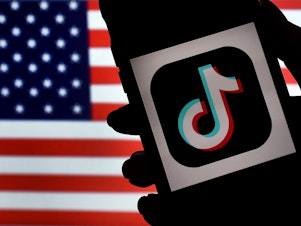caption: The social media application logo, TikTok is displayed on the screen of an iPhone on an American flag background. With the TikTok CEO set to testify on Capitol Hill on Thursday, influencers and lobbyists are pressing the government not to ban the app.