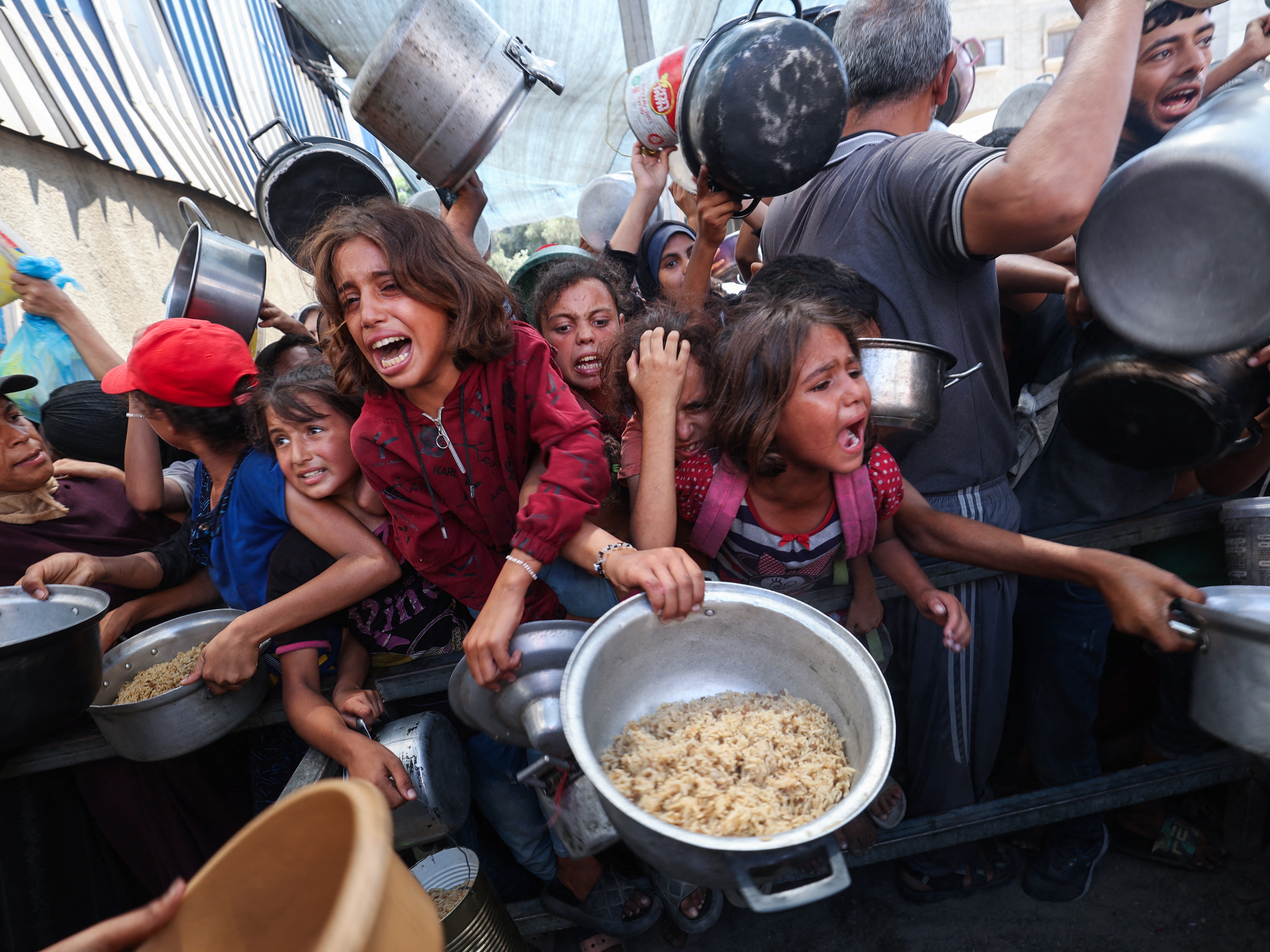 caption: Palestinians shove to receive a hot meal from a charity kitchen in the Nuseirat refugee camp in the Gaza Strip on Thursday.