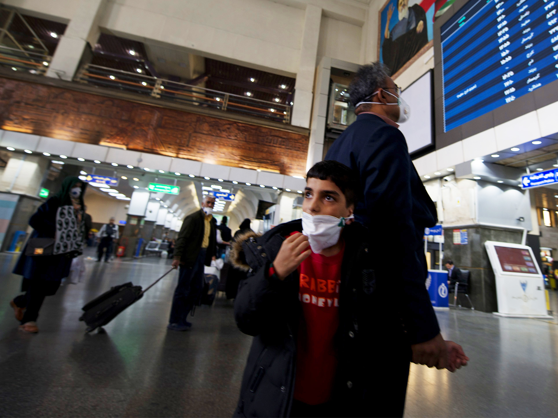 caption: A father holding his son's hand while checking the information board in a train station in Iran's capital, Tehran. Schools were closed and many public gatherings, including Friday prayers, were canceled as the coronavirus spread in Iran, even infecting senior officials.