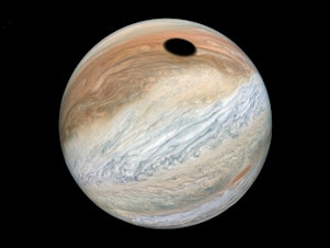 caption: This composite was made with images from NASA's Juno mission and shows the shadow on Jupiter cast by Io, one of its many moons.