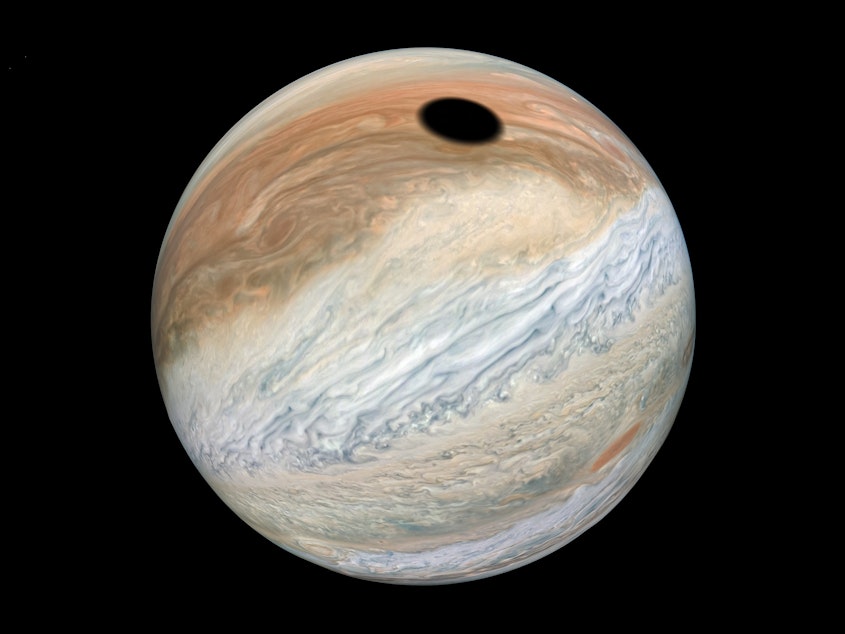 caption: This composite was made with images from NASA's Juno mission and shows the shadow on Jupiter cast by Io, one of its many moons.