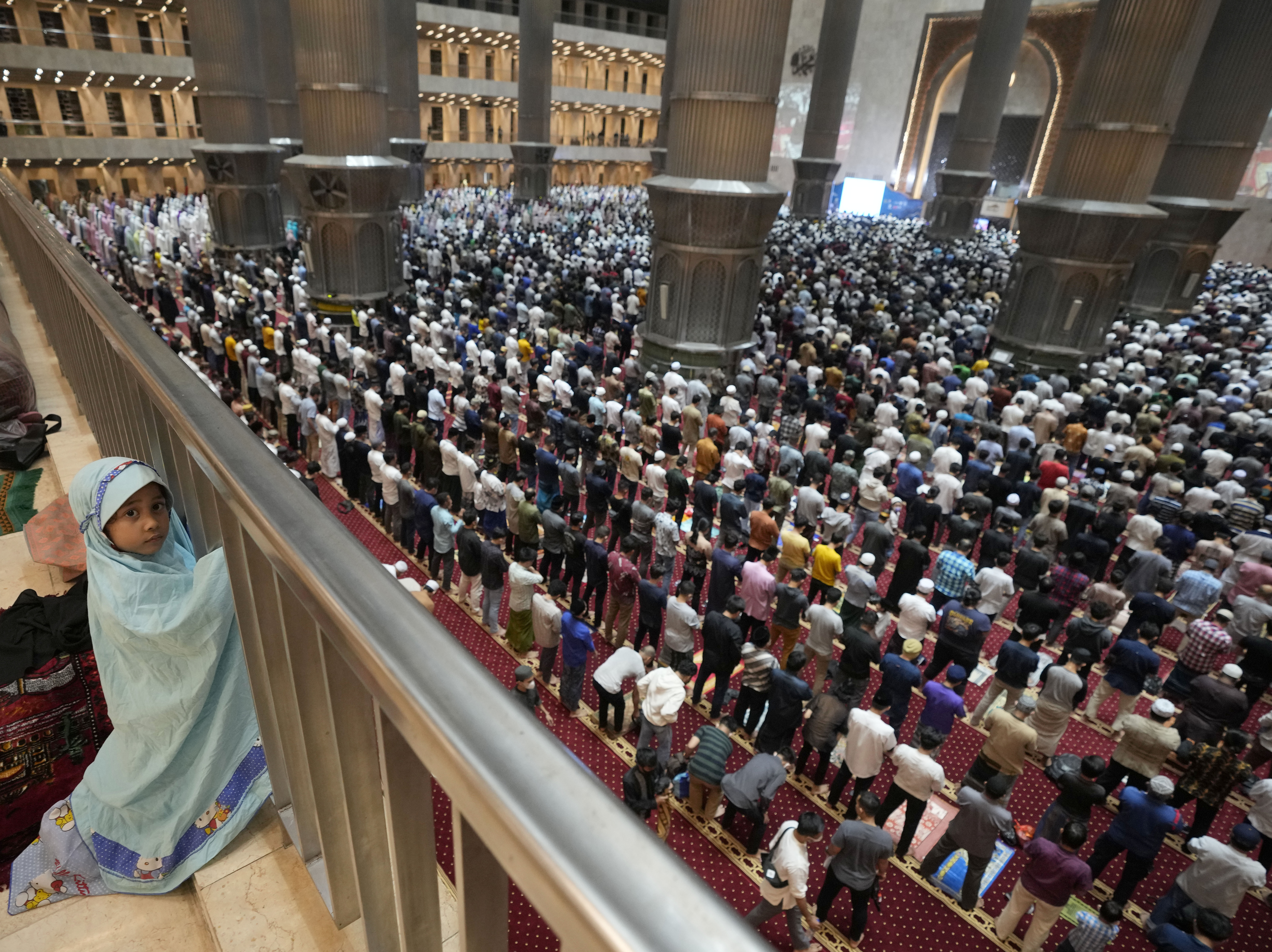 caption: A little girl looks on during an evening prayer on the eve of the holy fasting month of Ramadan at Istiqlal Mosque in Jakarta, Indonesia.