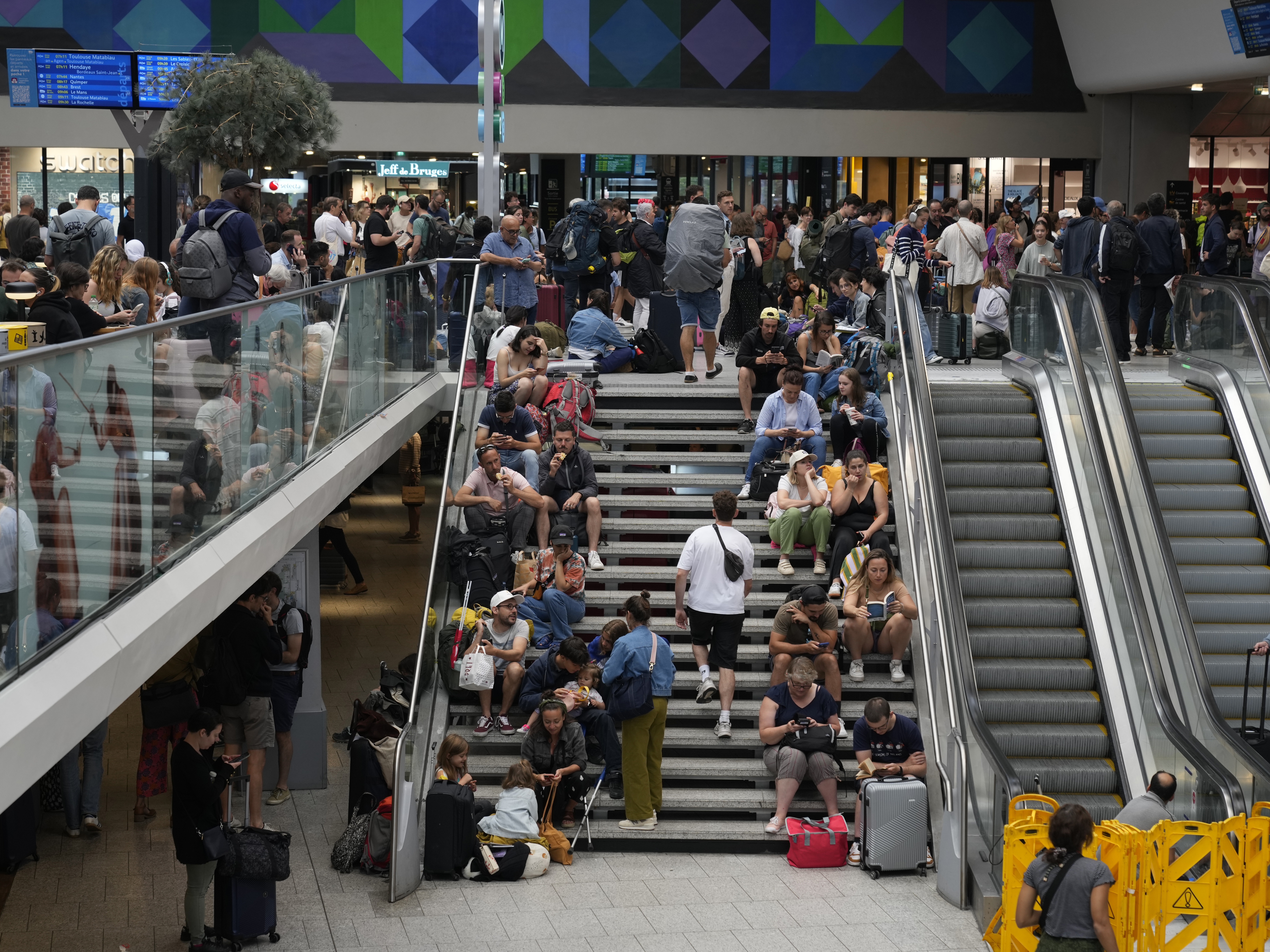 caption: Travelers sit on stairs at the Gare de Montparnasse at the 2024 Summer Olympics on Friday in Paris. Hours away from the opening ceremony of the Olympics, high-speed rail traffic to the French capital was severely disrupted on Friday following what officials described as "criminal actions" and sabotage.