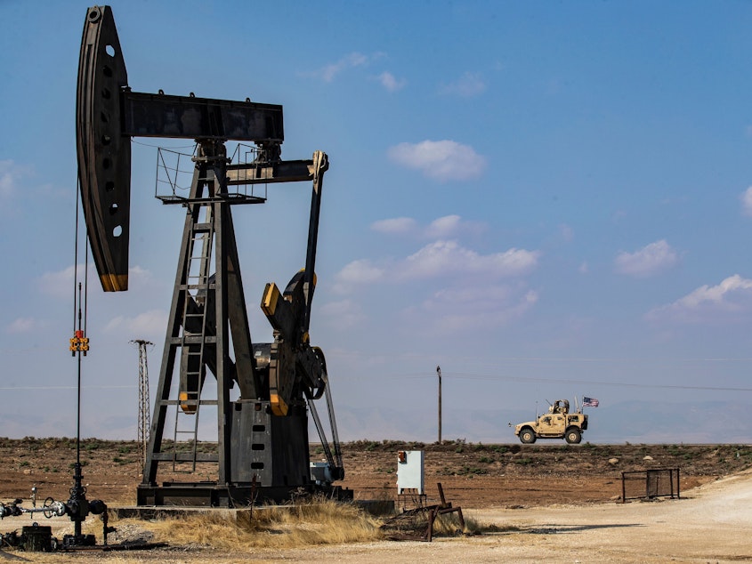 caption: A U.S. military vehicle drives past an oil pump jack in the countryside of Syria's northeastern city of Qamishli. President Trump is leaving some U.S. troops in Syria, with the goal of controlling Syria's oil fields. But legal experts say exploiting the oil could amount to pillaging — a war crime.