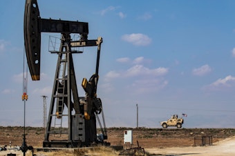 caption: A U.S. military vehicle drives past an oil pump jack in the countryside of Syria's northeastern city of Qamishli. President Trump is leaving some U.S. troops in Syria, with the goal of controlling Syria's oil fields. But legal experts say exploiting the oil could amount to pillaging — a war crime.